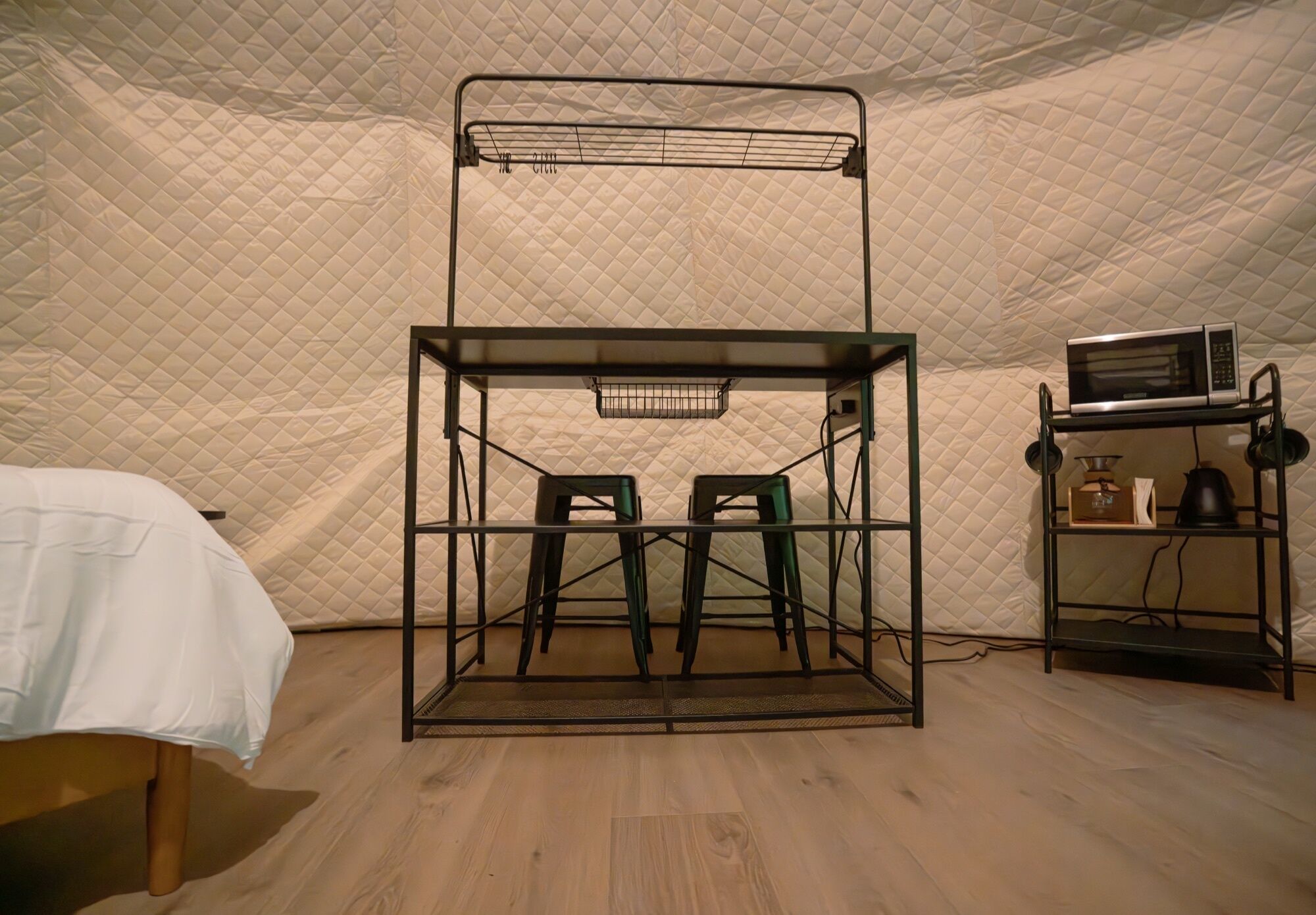 A tented room with a bunk bed, two chairs, a microwave, and a kettle.