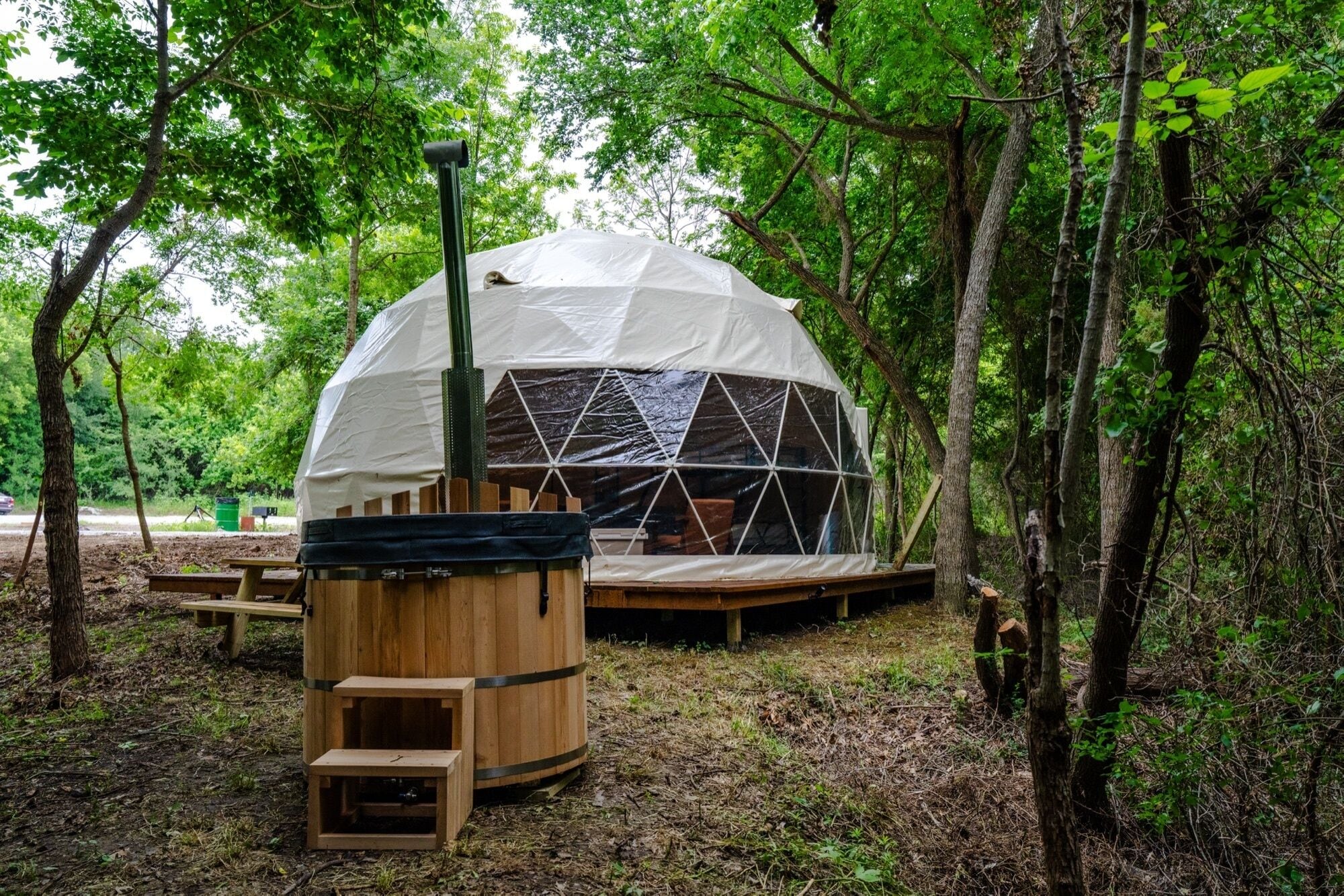 A geodesic dome structure in a forested area with a wooden bench and a small platform in front.