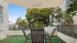An outdoor patio with a table and chairs, surrounded by a metal fence and greenery.
