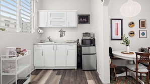 A compact kitchen with white cabinets, a stainless steel refrigerator, a microwave, and a dining area with a round table and chairs.