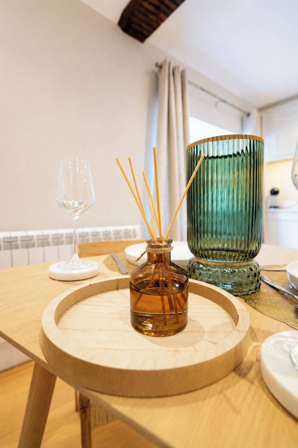 Een houten tafel met een glazen fles, een rietverspreider, een wijnglas en een groene glazen pot.