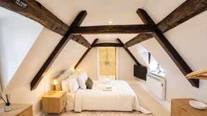 Ein Schlafzimmer mit schräg verlaufender Decke, einem Bett mit Kissen, Nachttischlampen, einem Nachttisch aus Holz und einem Schrank, sowie einem Fernseher an der Wand.