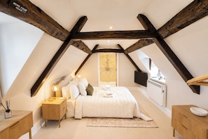 Ein Schlafzimmer mit schräg verlaufender Decke, einem Bett mit Kissen, Nachttischlampen, einem Nachttisch aus Holz und einem Schrank, sowie einem Fernseher an der Wand.