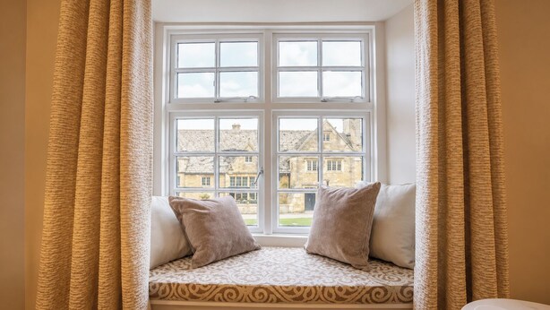 Ein Zimmer mit Fenster, einer Bank mit Kissen und Blick auf Gebäude.