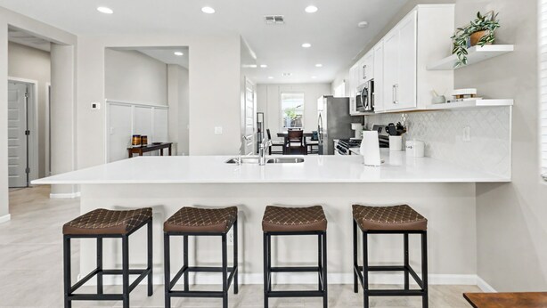 Una cocina moderna con una isla grande, taburetes de bar y armarios blancos.