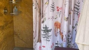 Un baño con cortina de ducha estampada con motivos naturales, una pared de madera y un estante con artículos de aseo.