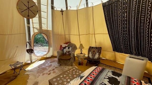 Interior de una tienda de campaña con una cama, una silla, una mesita y una ventana.