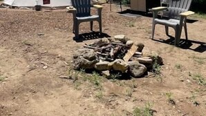 Un tipi con dos sillas, un pozo de fuego y una mesa con una parrilla en un área boscosa.