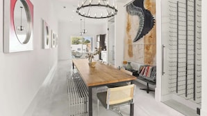 Un intérieur moderne avec une table à manger en bois, des chaises en métal, un lustre et un grand tableau abstrait.