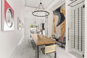 Ein modernes Interieur mit einem Holzespeisetisch, Metallstühlen, einer Chandelüster und einem großen, abstrakten Gemälde.