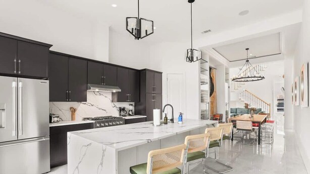 Une cuisine moderne avec des meubles de couleur sombre, un îlot en marbre, des appareils électroménagers en acier inoxydable et des tabourets de bar.