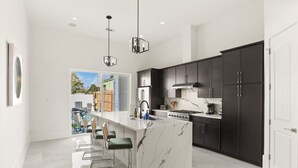 Une cuisine moderne avec un îlot en marbre, des meubles de couleur sombre et une vue sur l’extérieur.