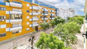 Un edificio amarillo de varios pisos con balcones, unidades de aire acondicionado y un patio empedrado con árboles.