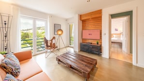 Una sala moderna con sofá, mesa de centro de madera, lámpara de pie y vistas al exterior.