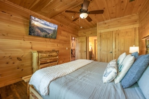 Ein Interieur einer Holzhütte mit einem Bett, einem Deckenventilator und einem Landschaftsbild.