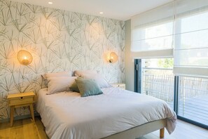 A bedroom with a bed, two wall-mounted lights, a nightstand, and a large window. - Apartment 50 metres from the sea (Penmarch)