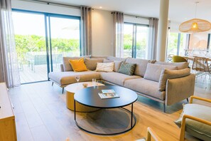 A modern living room with a sectional sofa, a round coffee table, and a dining area with a table and chairs. - Apartment 50 metres from the sea (Penmarch)