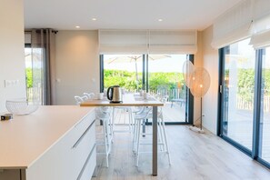 A modern kitchen with a central island, white bar stools, and large sliding glass doors leading to a deck. - Apartment 50 metres from the sea (Penmarch)
