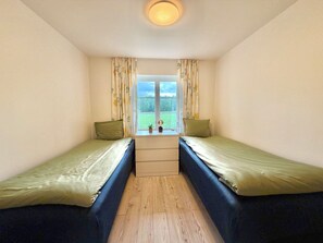 A small room with two single beds, a wooden floor, a window with curtains, and a ceiling light. - Large, lovingly renovated farmhouse – nature, hot tub, sauna, and boat (Olofström)