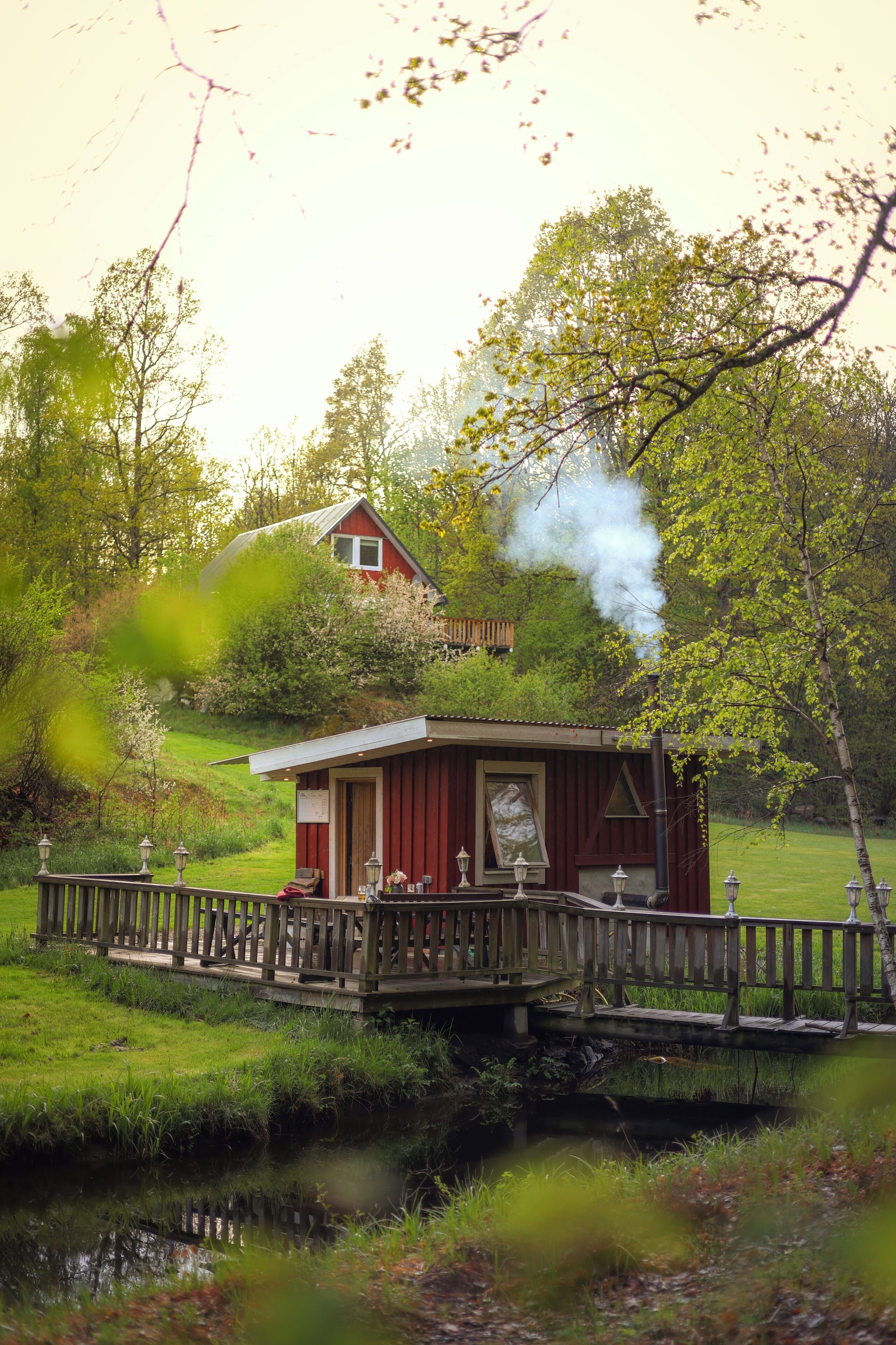 A small cabin with a dock, surrounded by greenery and a body of water.