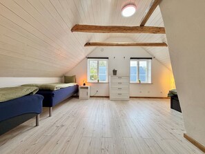 A room with a sloped ceiling, wooden beams, a bed with a blue mattress, a white dresser, and a window with a view. - Large, lovingly renovated farmhouse – nature, hot tub, sauna, and boat (Olofström)