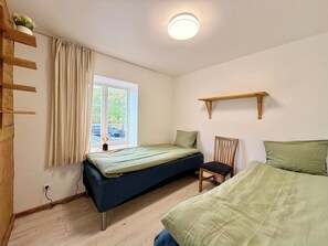 Een kamer met een bed, een stoel, een plank, een raam en een plafondlamp.