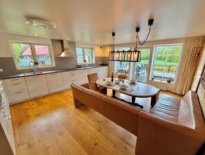 A modern kitchen with a central island, wooden flooring, and large windows offering views of the outdoors. - Large, lovingly renovated farmhouse – nature, hot tub, sauna, and boat (Olofström)