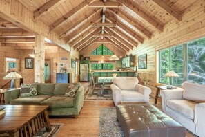 A log cabin interior with a high ceiling, wooden walls, a dining area, and a large window. - Mountain Magic | Hot Tub, Game Room, Near Parkway, Dollywood & National Park (Sevierville)