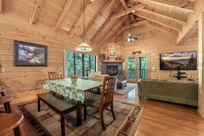 A wooden cabin interior with a dining table, chairs, a sofa, a fireplace, and a television. - Mountain Magic | Hot Tub, Game Room, Near Parkway, Dollywood & National Park (Sevierville)