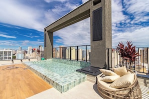 A rooftop terrace with a swimming pool, a lounge chair, and a view of the city skyline. - Edifício Morá (Curitiba)