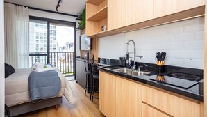 A compact kitchen with a black countertop, wooden cabinets, and a built-in sink. - Edifício Morá (Curitiba)