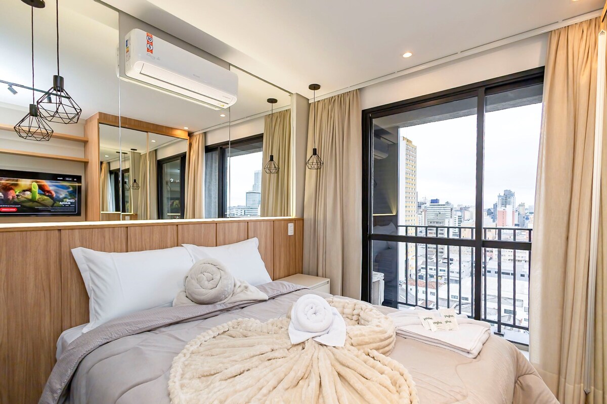 Habitación de hotel con cama, ventana grande, aire acondicionado y vista a la ciudad.