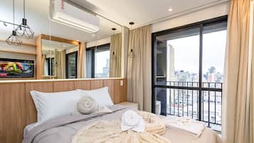 A hotel room with a bed, a large window, an air conditioning unit, and a city view.