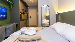 A hotel room with a bed, a desk, a TV, a mirror, and a door leading to a bathroom. - Edifício Morá (Curitiba)