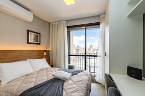 Quarto de hotel com cama, escrivaninha, vista da cidade e ar condicionado.