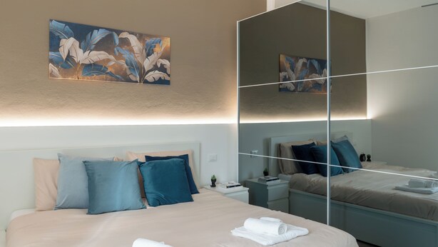 A modern bedroom with a large bed, bedside tables, a nightstand, a mirror, and artwork on the wall. - From Kri•Modern design - 10 min Orio al Serio airport Bergamo - Self check in (Seriate)