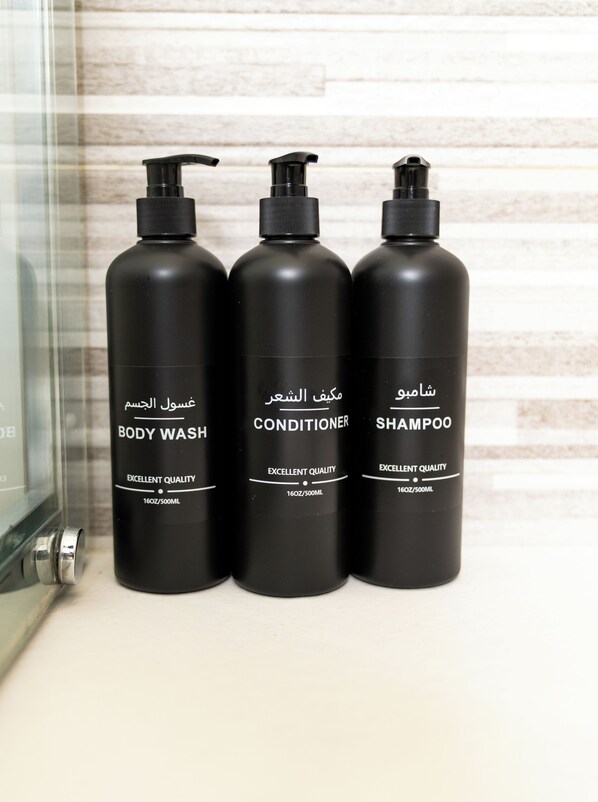 Three black bottles of body wash, conditioner, and shampoo with Arabic text and 'EXCELLENT QUALITY' on a countertop.