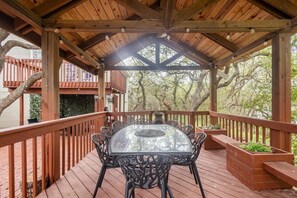 Eine überdachte Terrasse im Freien mit einem Tisch und Stühlen mit Glasplatte, umgeben von Holzgeländern und Blick auf Bäume.
