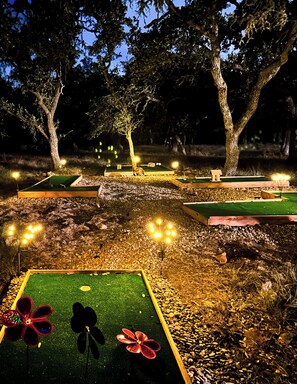 Een buitenruimte bij nacht met verschillende minigolfbanen, verlicht door kleine lantaarns.