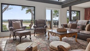 A spacious living room with large windows, a fireplace, and a view of the outdoors. - Lakefront Home w/Views, Huge Deck, Family-Friendly (Lago Vista)