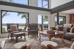 A spacious living room with large windows, a fireplace, and a view of the outdoors. - Lakefront Home w/Views, Huge Deck, Family-Friendly (Lago Vista)