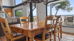 A dining area with a wooden table and chairs, a chandelier, and large windows with a view. - Lakefront Home w/Views, Huge Deck, Family-Friendly (Lago Vista)