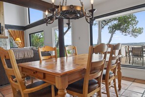 A dining area with a wooden table and chairs, a chandelier, and large windows with a view. - Lakefront Home w/Views, Huge Deck, Family-Friendly (Lago Vista)