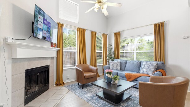 A living room with a fireplace, a television mounted on the wall, a ceiling fan, and a sofa. - Enfilar Lane: Cozy Retreat Close to Stadiums & DFW (Arlington)