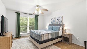 A bedroom with a bed, a TV, a desk, a ceiling fan, and artwork on the wall. - Enfilar Lane: Cozy Retreat Close to Stadiums & DFW (Arlington)