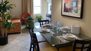 Un coin repas avec une table dressée pour quatre personnes, des chaises, une plante en pot, un canapé et un tableau accroché au mur.