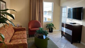 Un salon comprenant un canapé, un fauteuil, une table basse avec une plante, un téléviseur et une commode.