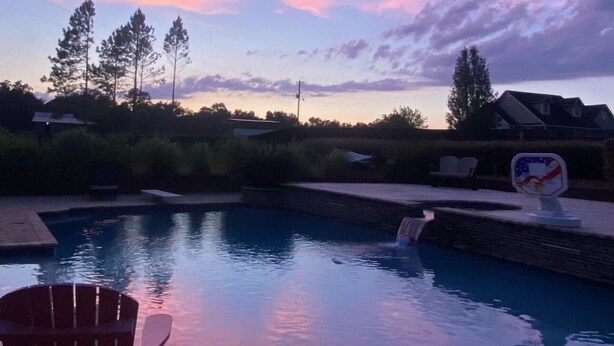 A swimming pool with a chair, surrounded by trees and a house in the background. - Delightful 1-bedroom poolside house with AC in charming Hahira. (Hahira)