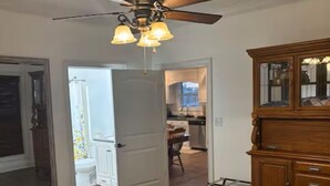 A bedroom with a bed, a ceiling fan, a wooden dresser, and a view into the kitchen. - Delightful 1-bedroom poolside house with AC in charming Hahira. (Hahira)