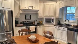 A kitchen with white cabinets, a wooden dining table, and a stainless steel refrigerator. - Delightful 1-bedroom poolside house with AC in charming Hahira. (Hahira)